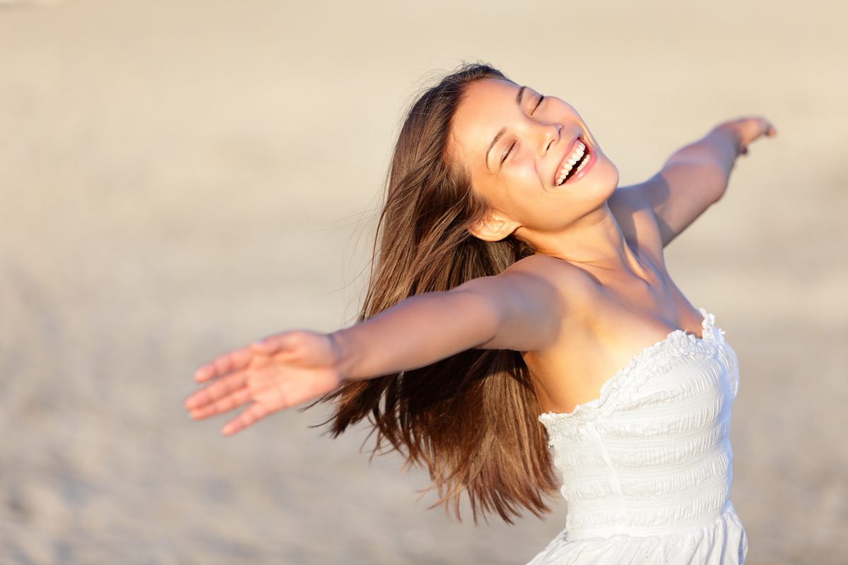A woman with arms spread wide, laughing in the sun